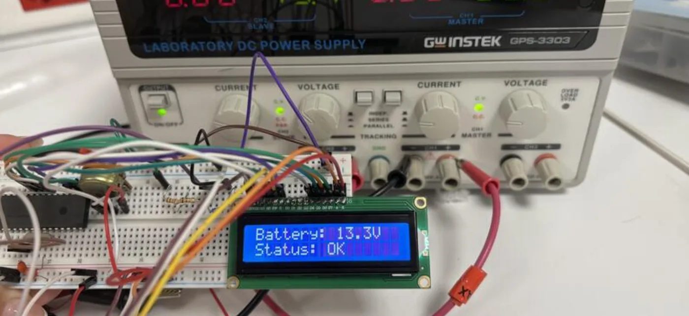 The prototype on a breadboard: a PIC microcontroller wired to a 16×2 LCD reading ‘Battery: 13.3V, Status: OK’, powered from a bench supply